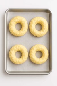 Unbaked cottage cheese bagels shaped into rings on a baking sheet lined with parchment paper