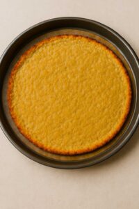 Freshly baked ground chicken pizza crust, golden and firm, cooling on a round pan.