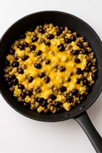 Scrambled eggs, turkey sausage, black beans, and melted cheese in a skillet for high protein breakfast burrito