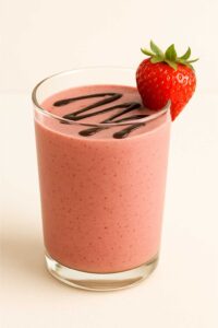 Glass of chocolate covered strawberry protein shake with chocolate drizzle and a fresh strawberry garnish.