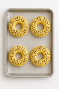 Unbaked cottage cheese bagels topped with everything bagel seasoning on a parchment-lined baking sheet