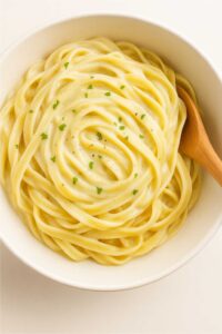 pasta fully coated in creamy white cottage cheese sauce, garnished with fresh parsley and black pepper, in a white bowl with a wooden spoon : cottage cheese and pasta sauce​