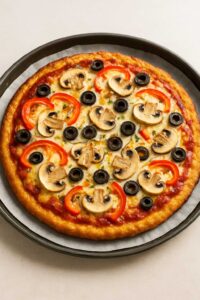 Freshly baked ground chicken pizza crust topped with tomato sauce, cheese, mushrooms, olives, and red peppers.