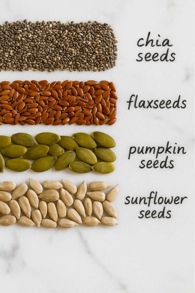 Four lines of seeds—chia, flax, pumpkin, and sunflower—arranged on a marble surface with handwritten labels, illustrating the bariatric seed recipe.