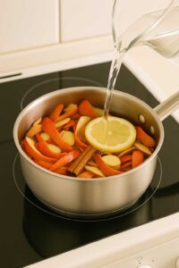 Pouring water into a saucepan filled with apple peels, ginger slices, a cinnamon stick, and a lemon slice to start the apple peel recipe for weight loss.
