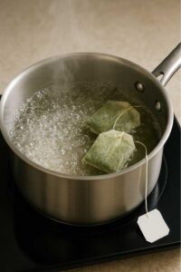 Boiling water in a saucepan with two green tea bags steeping on a stovetop for green tea lemonade