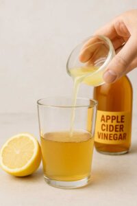 A hand pouring fresh lemon juice from a small glass bowl into a glass of apple cider vinegar. the first step to prepare natural ozempic recipe