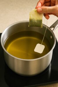 Hand removing a green tea bag from a saucepan of brewed tea for preparation green tea lemonade