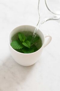 Hot water being poured over lemon balm leaves in a white mug for a lemon balm for weight loss recipe.