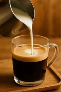 Steamed half-and-half is slowly poured from a frothing pitcher into a glass mug of espresso, creating the classic breve coffee blend.