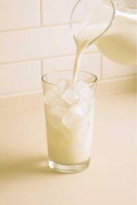 Milk being poured into a tall glass of ice for an iced matcha latte.