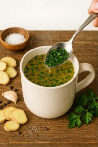 Adding fresh parsley to a steaming mug of homemade ginger, garlic, and lemon broth—final step for natural sulphur burps zepbound relief.