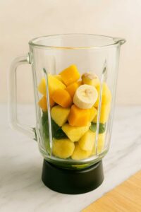 Frozen fruits layered over greens in blender for Detox Island Green Smoothie